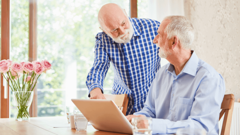 two old men looking at a laptop on a table